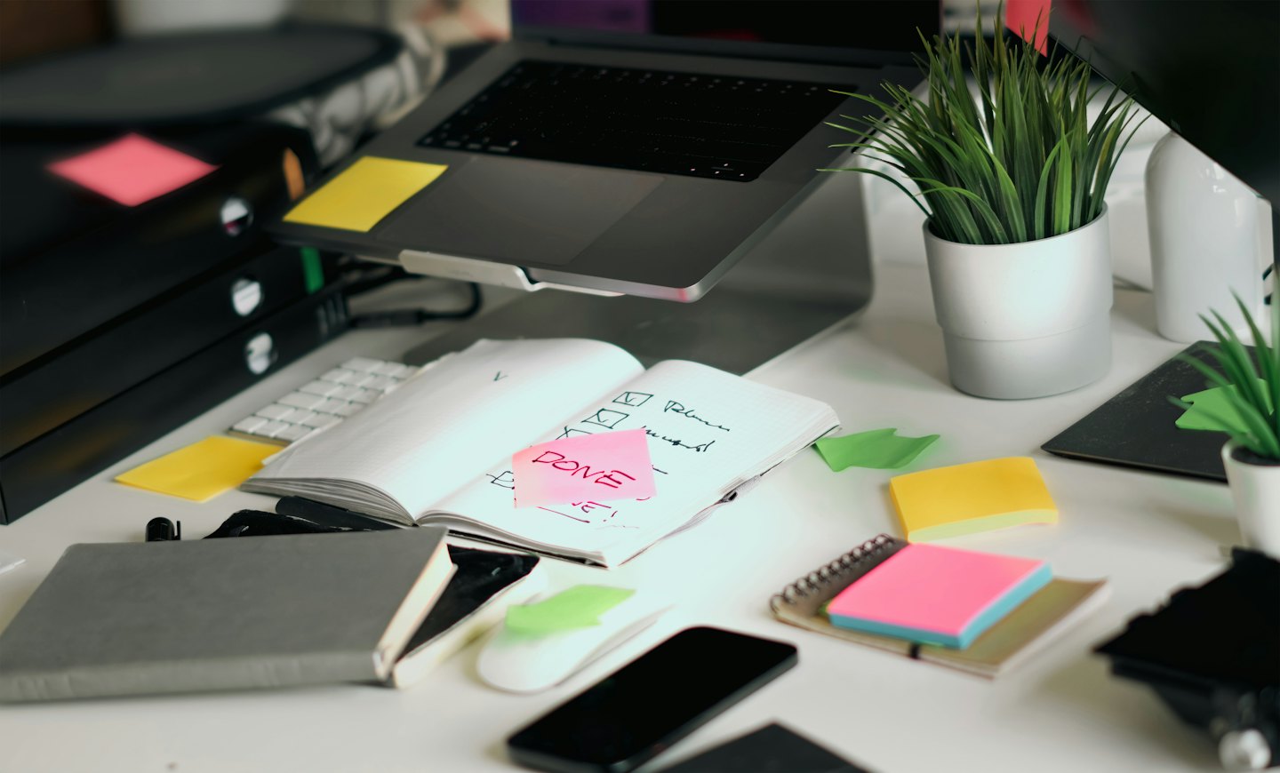 A laptop and handwritten checklist on a cluttered desk.